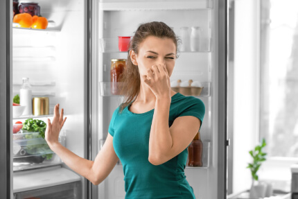 Frau hält sich wegen schlechtem Geruch aus Kühlschrank die Nase zu