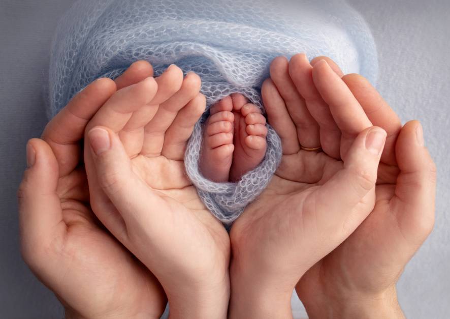 Hände von Eltern in Herzform um Babyhände gelegt